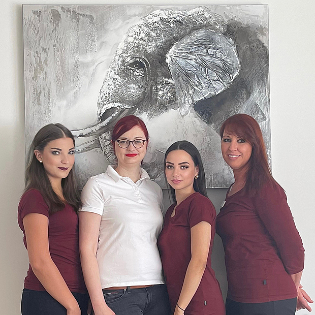4 Frauen jungen und mittleren Alters in Teamkleidung, lächelnd, stehend vor Wandbild mit Elefant